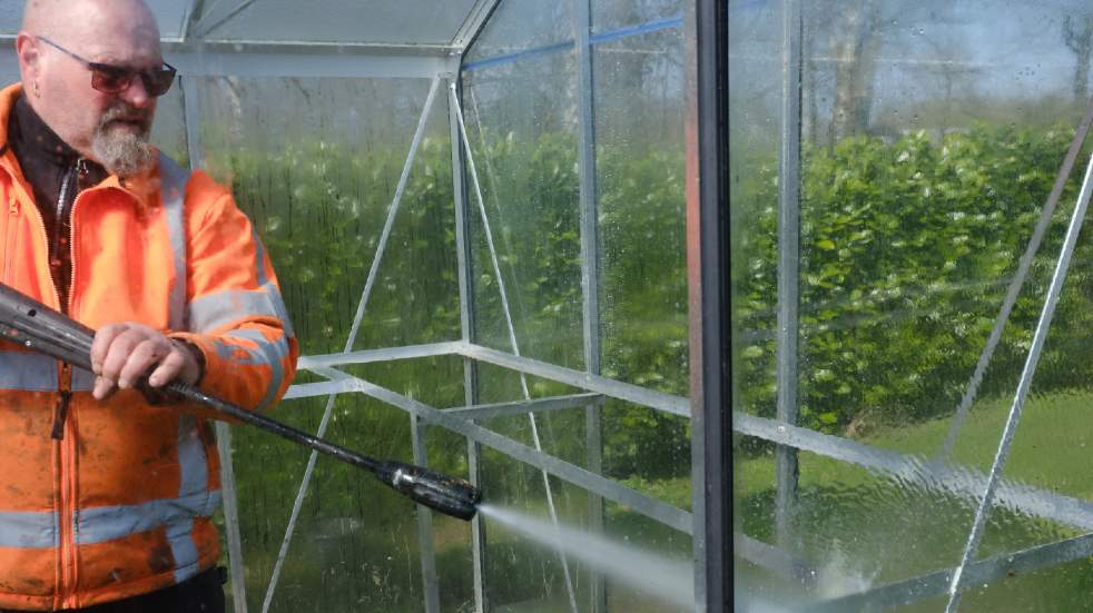 Get your garden ready for the summer man hosing greenhouse